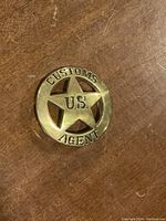 Front of round brass belt buckle with star cutout and raised text "CUSTOMS U.S. AGENT" on wooden surface.