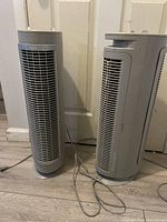 Two upright Holmek filtering fans with visible power cords and front grilles placed side by side, showing overall shape and size.