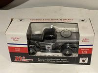 Front view of the coin bank in its original white display box with a clear window showing the black die cast model truck and product details like 'Locking Coin Bank With Key', 'Die Cast Metal', '10th Anniversary Edition', '1/25th Scale'.