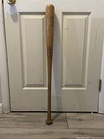 Full view of the wooden Louisville Slugger baseball bat standing upright against a door.