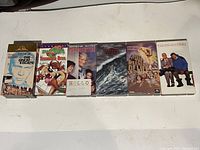 6 VHS movie tapes lined up on a white surface, titles visible.