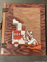 Front cover of wooden journal showing decorative inlay of reclining figure and house motif, latch binding visible.