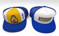 Two vintage trucker hats with patches and logos: left hat has '43 Squadron' crest with crown and maple leaf, right hat has 'Homes' logo in blue and yellow on white front panel.