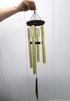 Hand holding the Arias wind chime showing full length and components including anodized aluminum tubes and finished redwood top.