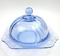Blue translucent glass butter dish with a square base and matching domed lid. Embossed floral and scroll designs on surface, rounded lid knob.