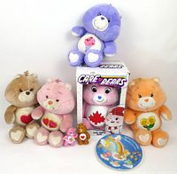 Six Care Bears plush toys including a boxed 2003 True North Bear plush, orange, pink, brown plush bears, and two mini 80s figures. Also visible is a colorful round Care Bears cake plate.