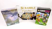 Three boxed games: Dragonrealm boxed in shrinkwrap, Harry Potter Scrabble with Harry Potter themed box, FunkoVerse Disney Alice in Wonderland sealed boxed game.