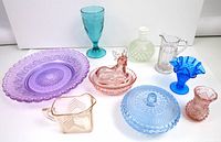 Full lot with various pressed glass items in multiple colors including green, purple, pink, blue, and white hobnail bottle.
