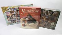 Front view of three puzzle boxes: Coronation Street double-sided puzzle, Sweet Revenge mystery puzzle, Cobble Hill deer puzzle.