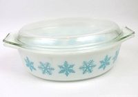 White milk glass Pyrex casserole dish with turquoise snowflake design and clear glass lid on top, viewed from above.