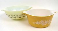Two bowls side by side: rear Bowl in cream/pale yellow with gold/grey floral Butterfly Gold pattern; front bowl in mustard yellow with white floral Wild Rose pattern