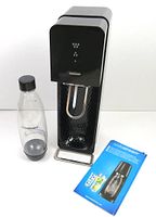 Shows the SodaStream carbonation machine, the 1L bottle, and the instruction guide pamphlet arranged together