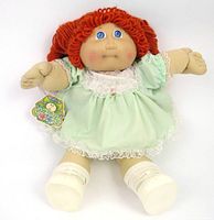 Full front view of the vintage 1984 Cabbage Patch Kids doll with red yarn hair and blue eyes wearing a mint green dress and white shoes, original tag attached.