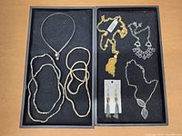 Top down image of two black trays containing assorted jewelry pieces including necklaces, bracelets, and earrings in various metallic and beaded styles.