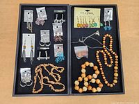 Two trays showing various earrings and wooden bead necklaces in trays on a surface