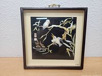 Shadowbox artwork showing three white birds on tree branch over water, framed in brown wood with hanging handle.