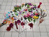 Overview of assorted artificial flowers and decorative items laid on tile floor.