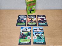 Five children's books from The Gameknight999 vs Herobrine series arranged on white surface with original collection box behind them.