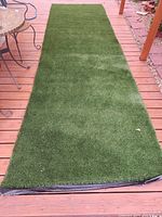 Full view of rectangular artificial grass piece laid on wooden deck showing texture and condition.