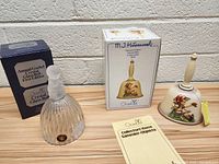 Two Goebel collectible bells, one crystal glass and one ceramic with painted Hummell figure, with their original boxes and a collectors item card.