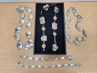 Four vintage silver-toned belts with ornate embossed designs, shown laid flat on a wooden surface