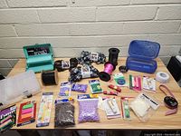 Overview of assorted craft materials and tools on a wooden table with a concrete block wall background