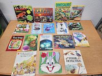 Photo shows a group of 18 assorted kid's books arranged on a table with various colorful covers showing animals, dinosaurs, adventures, and school themes.