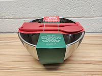 Stainless steel bowl with three red silicone utensils resting on top, all new with tags.