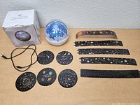 Star light projector dome with various flat celestial disc and band projection accessories, power cable and product box on a white surface.