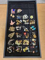 Tray with multiple compartments containing mostly paired earrings in various designs, colors, and materials.