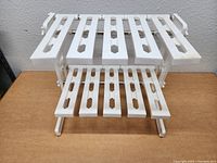 White plastic under sink organizer rack photographed from front angle showing two-tier slotted design and adjustable arms.