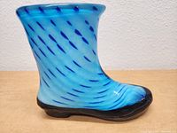 Blue glass boot figurine shown from side profile depicting swirling blue pattern and black base.