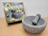 Large stone mortar and pestle shown with original box behind it on wooden surface.