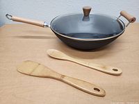 Wide angle photo showing the large wok with glass lid and two bamboo utensils laid in front of it