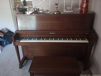 Front view of the large Baldwin upright piano with the keyboard exposed and matching wooden bench in front.