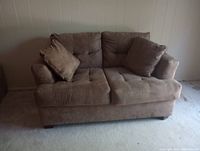 Front view of brown loveseat sofa with two cushions on light carpeted floor against plain wall.