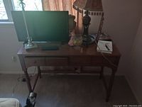 Wooden desk with items on top including a monitor, lamp, and small decorative objects.