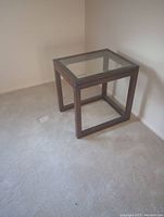 Wooden end table with glass top, viewed from an angle showing the design and condition.