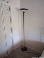 Tall black upright lamp standing against wall