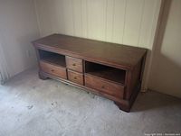 Photo of brown wooden TV stand showing front view with visible 4 drawers and 2 shelves.