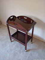 Wooden end table with removable tray top with curved folding edges, dark wood finish, and brass casters