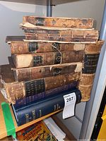 Stack of nine books on shelf including seven small leather volumes and two blue cloth hardcovers
