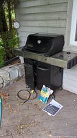 Black Weber gas grill with side shelves, manual and bag of wood chips placed in front