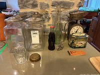 Wide shot of all lot items arranged on countertop including postal scale, glass canisters, Coca-Cola bottles, biscuit tin, cookie cutters, and coupon book