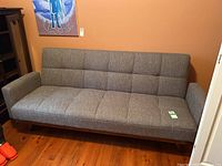 Front view of gray fabric convertible sofa bed against an orange wall, showing tufted seat and back