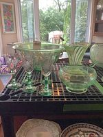 Photo of green Depression glass items including large mixing bowl, centerpiece vase, small bowl, and stemmed glasses on table.