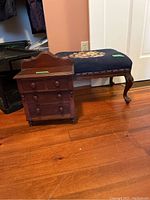 Miniature dresser and embroidered-top footstool displayed side by side on hardwood floor