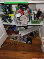 Photo of shelves with various baskets and items including light bulbs, tape, spray cans, cords, and a wooden tool carrier on floor