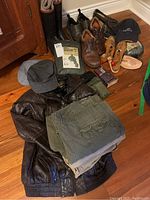 Photo shows all items including leather jacket, rain suits still in packaging, cargo shorts, hats, shoes, rubber boots, shoe stretchers, wallet, and travel shave pack.