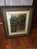 Full view of the framed painting leaning against a brick wall, showing ornate carved frame and visible painting details.